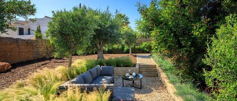 A landscaped outdoor area with a gray sofa, a small table, and a stone wall.