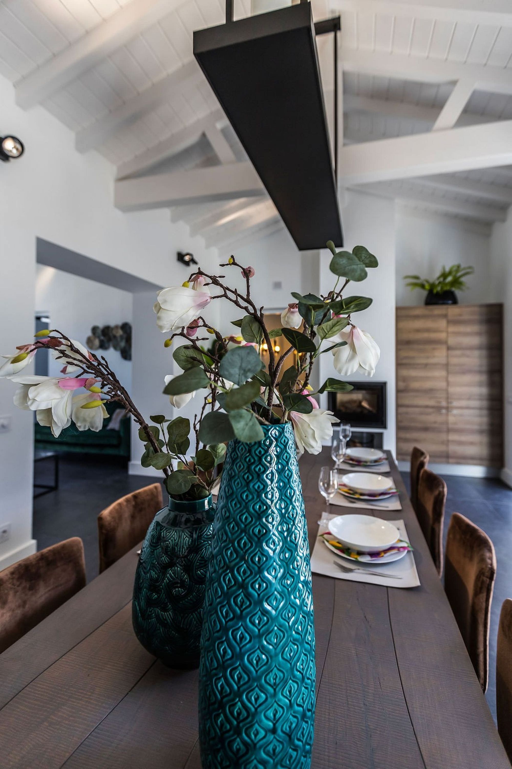 Un tavolo da pranzo con due vasi di fiori, un armadietto in legno e una televisione sullo sfondo.