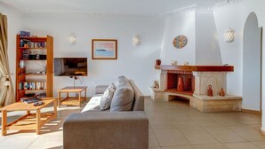 A living room with a sofa, coffee table, bookshelf, TV, fireplace, and decorative items. - 11 Marinha Two Bedroom Apt at Praia do Marinha (Lagoa)