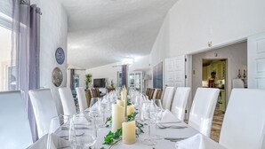 Un comedor con una larga mesa dispuesta para una comida, sillas blancas y velas.