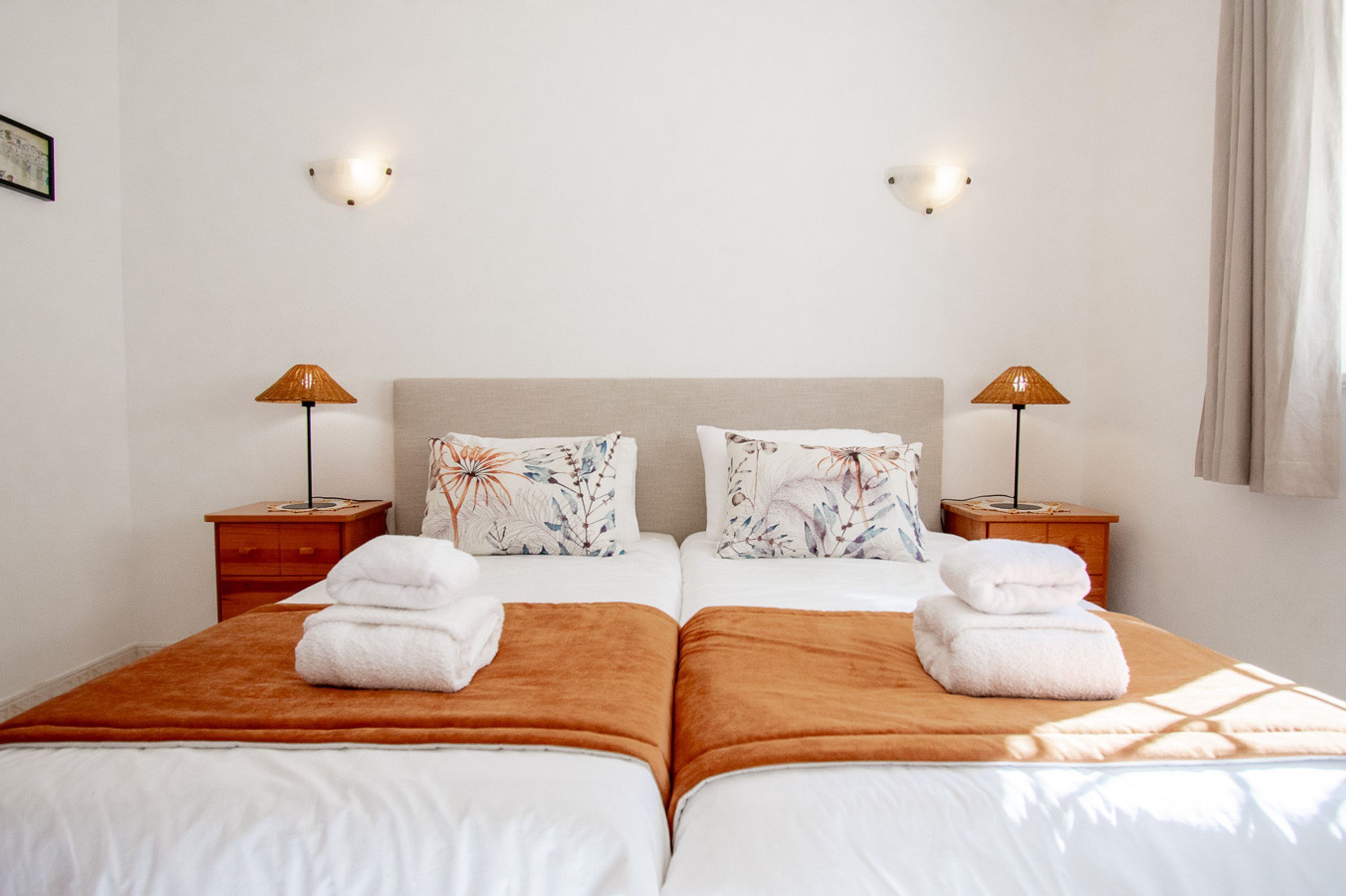 Een tweepersoonsbed met twee kussens, een nachtkastje, een lamp en een raam met gordijnen.