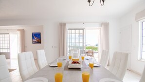 A dining room with a long table set for breakfast, white chairs, and orange juice glasses. - Casa Filipa Lower Floor (Lagoa)