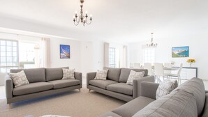A modern living room with two grey sofas, a coffee table, and a dining area with a white table and chairs. - Casa Filipa Lower Floor (Lagoa)