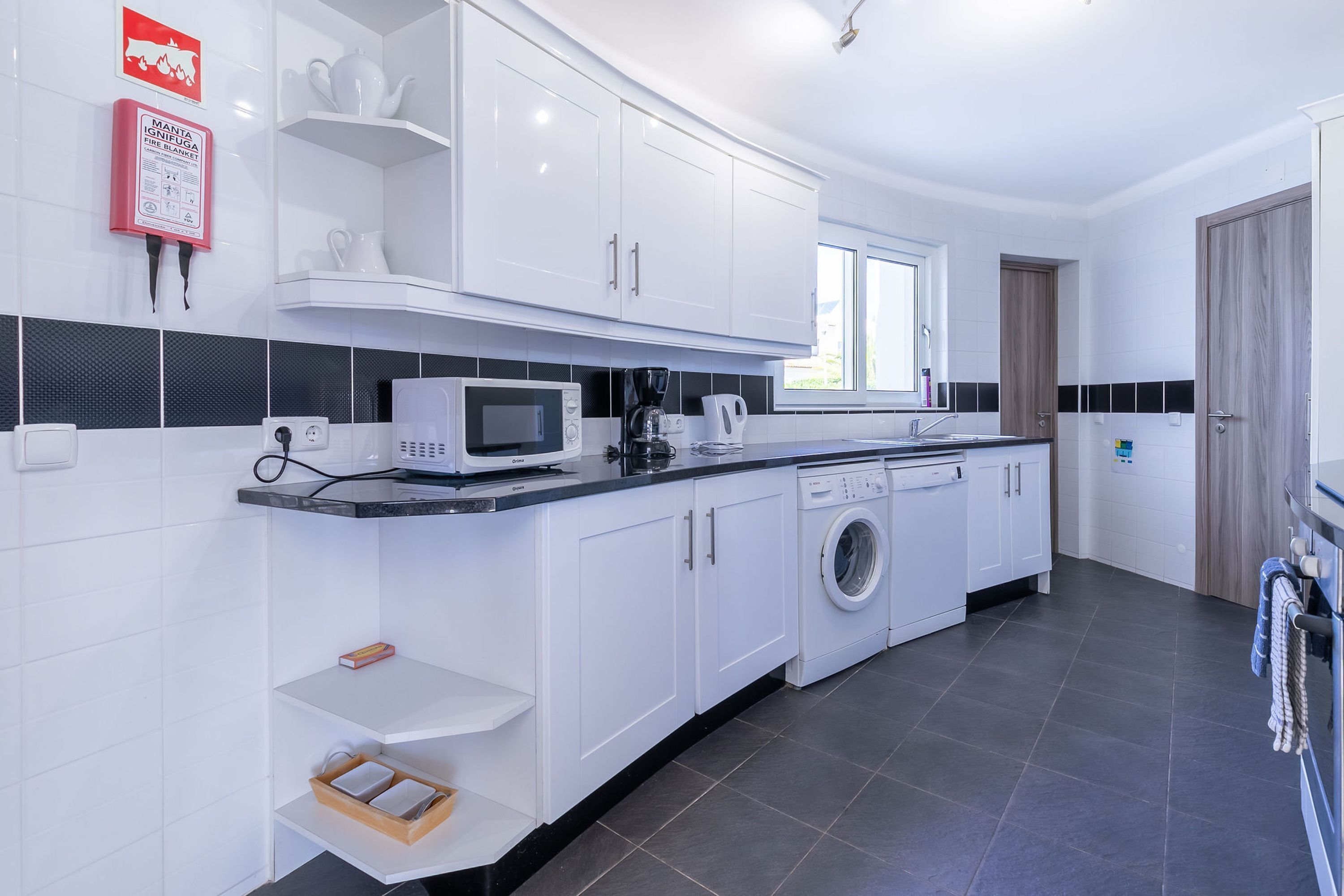 A modern kitchen with white cabinets, a microwave, a coffee maker, and a washing machine.