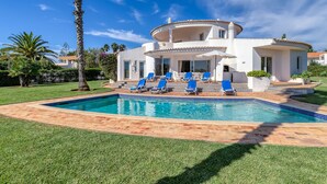 Una casa a due piani con piscina, poltrone da relax blu e un prato ben curato.