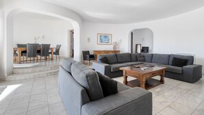 Un soggiorno moderno con un divano ad angolo grigio, un tavolino in legno e un'area pranzo con tavolo e sedie in legno.