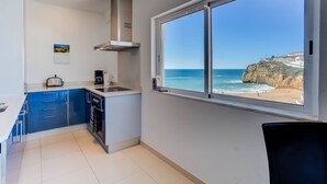 Une cuisine moderne avec des armoires bleues, une hotte de cuisinière en acier inoxydable et une grande fenêtre donnant sur une plage.