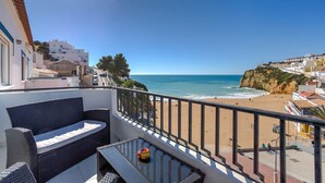 Un balcon meublé avec des meubles en osier, offrant une vue sur une plage et les bâtiments situés sur la falaise.