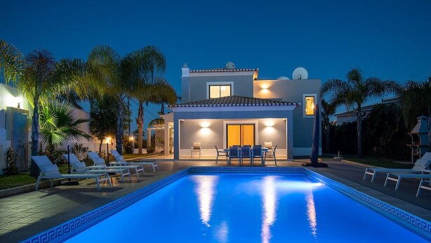 A modern house with a swimming pool, lounge chairs, and a well-lit patio area. - Albatroz Gorgeous Spacious Villa IN Carvoeiro (Lagoa)