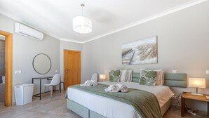 A modern bedroom with a large bed, a desk, a chair, and a wall-mounted air conditioner. - Albatroz Gorgeous Spacious Villa IN Carvoeiro (Lagoa)