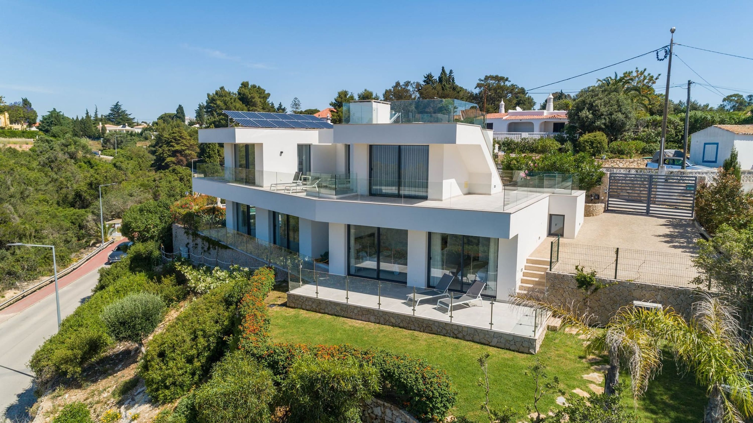 A modern two-story house with a flat roof, large windows, and a solar panel.