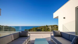 Un espacio de estar moderno al aire libre con vista al mar y vegetación.