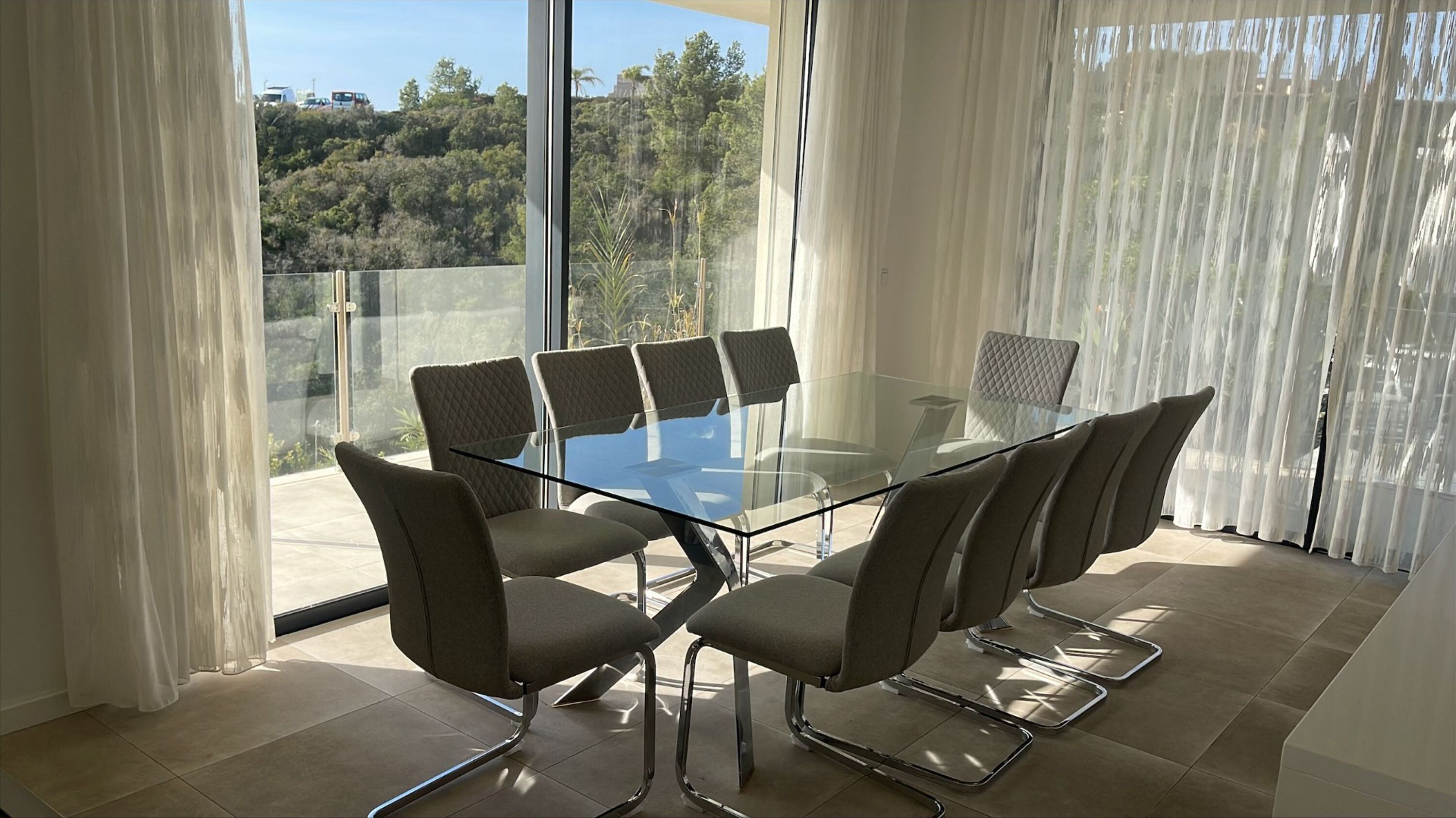 Une salle de réunion moderne, dotée d’une table en verre et de six chaises, de grandes fenêtres avec des rideaux légers et offrant une vue sur une colline boisée.