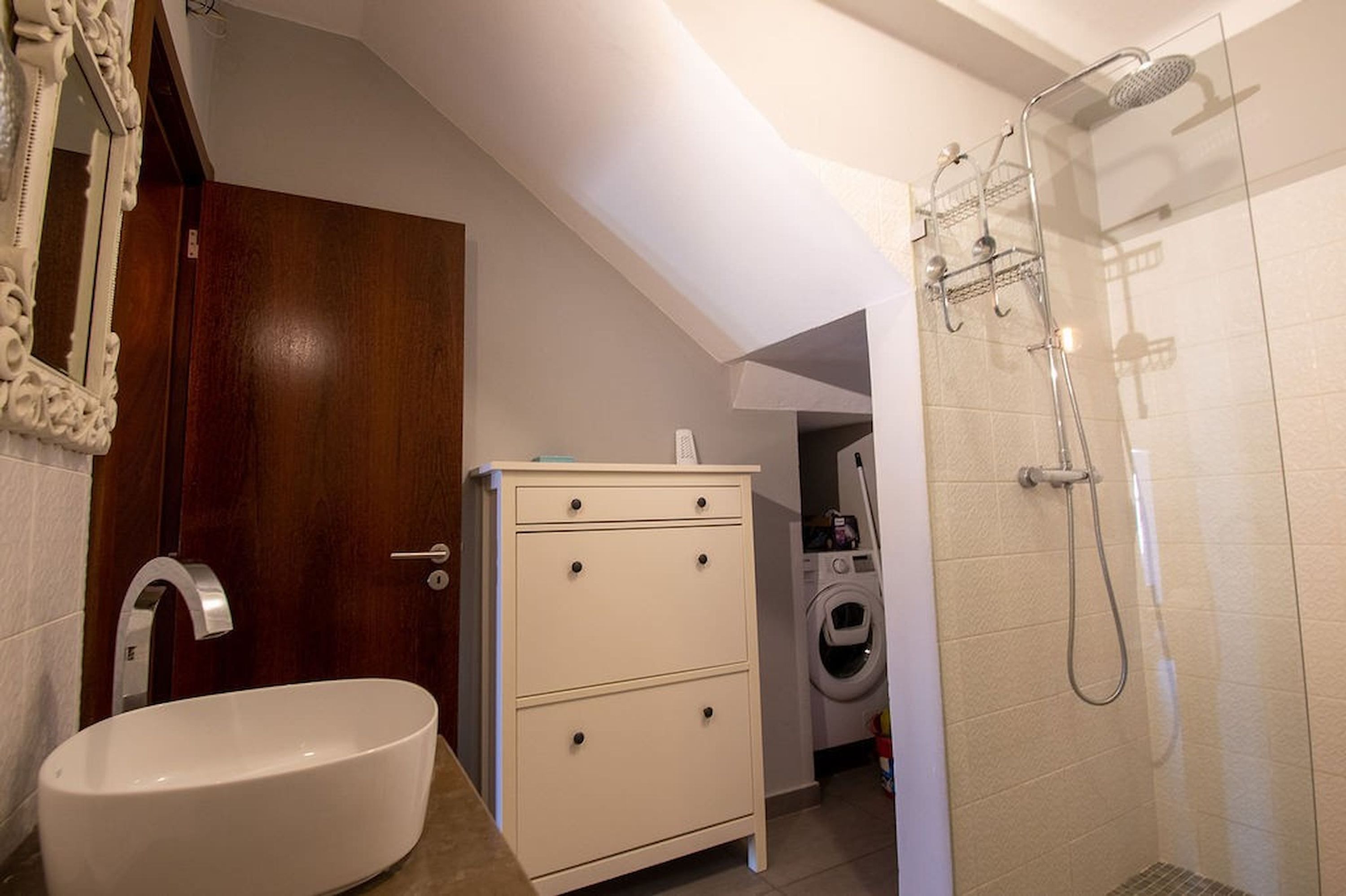 Un bagno con lavandino, mobile, doccia e lavatrice sullo sfondo.