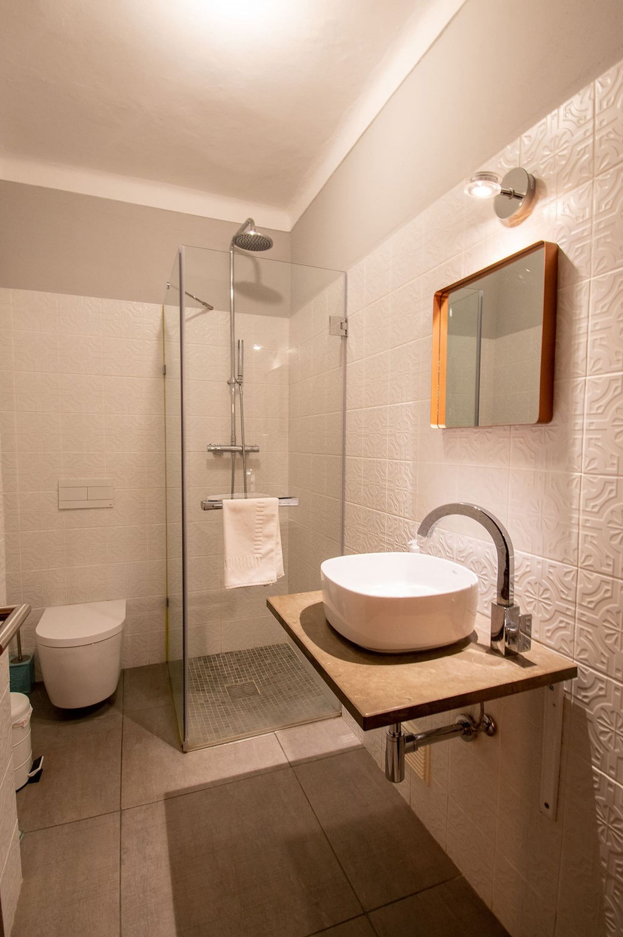 A modern bathroom with a glass-enclosed shower, a round sink with a wooden countertop, and a wall-mounted mirror.
