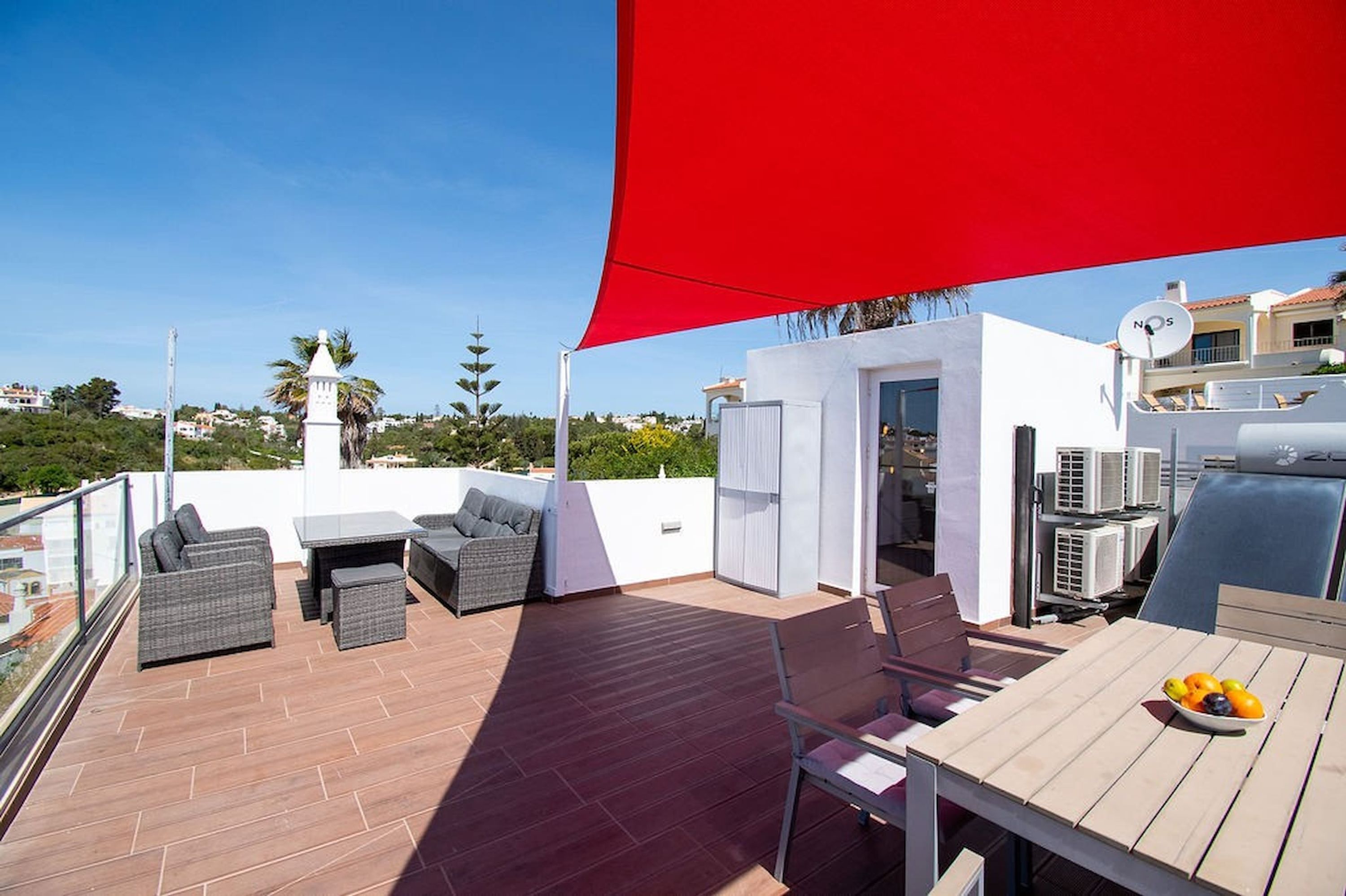 Une terrasse sur le toit, aménagée avec du mobilier d’extérieur, une table garnie de fruits et un auvent rouge.