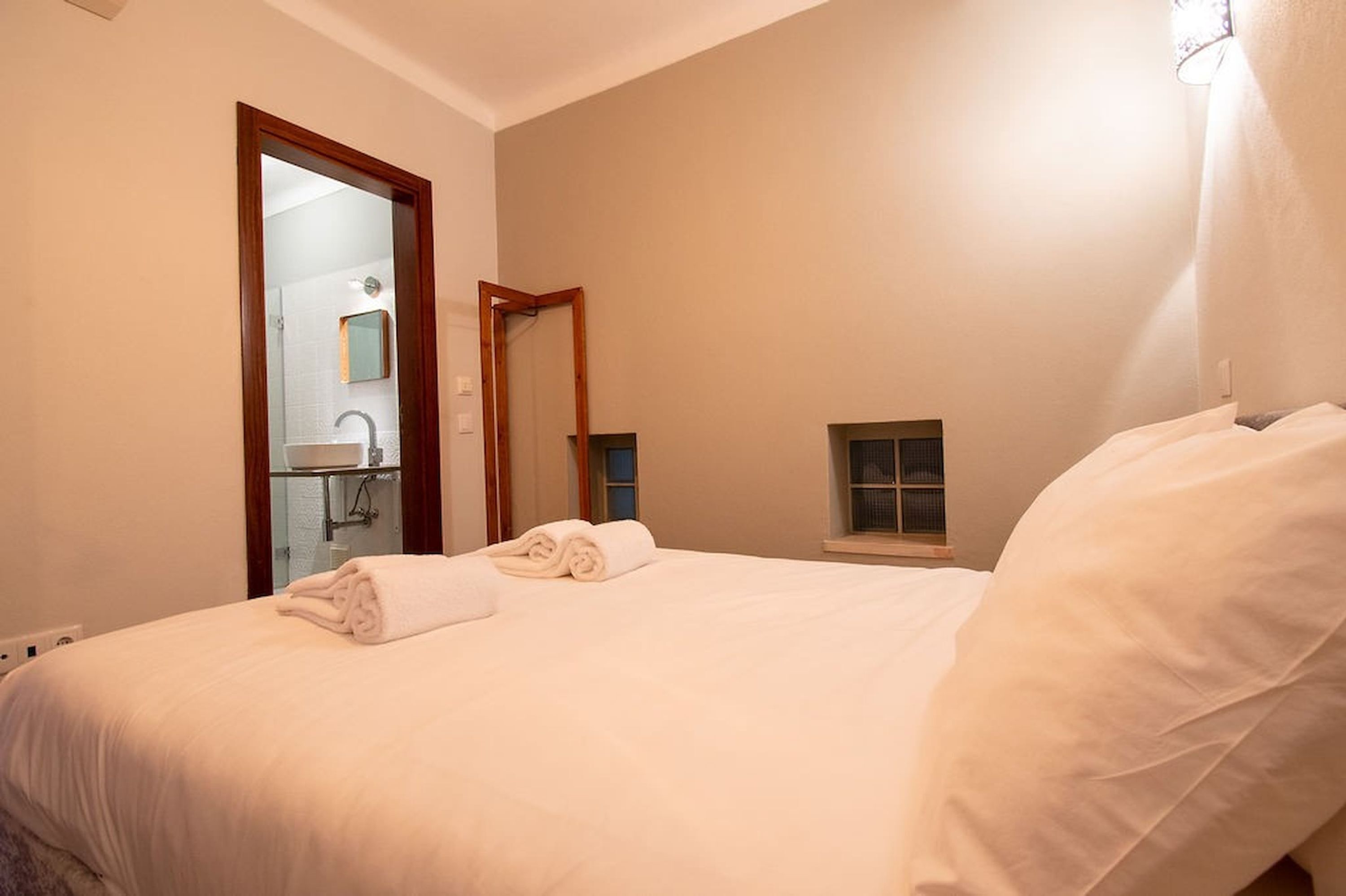 A hotel room with a bed, a bathroom visible through an open door, and a small window.