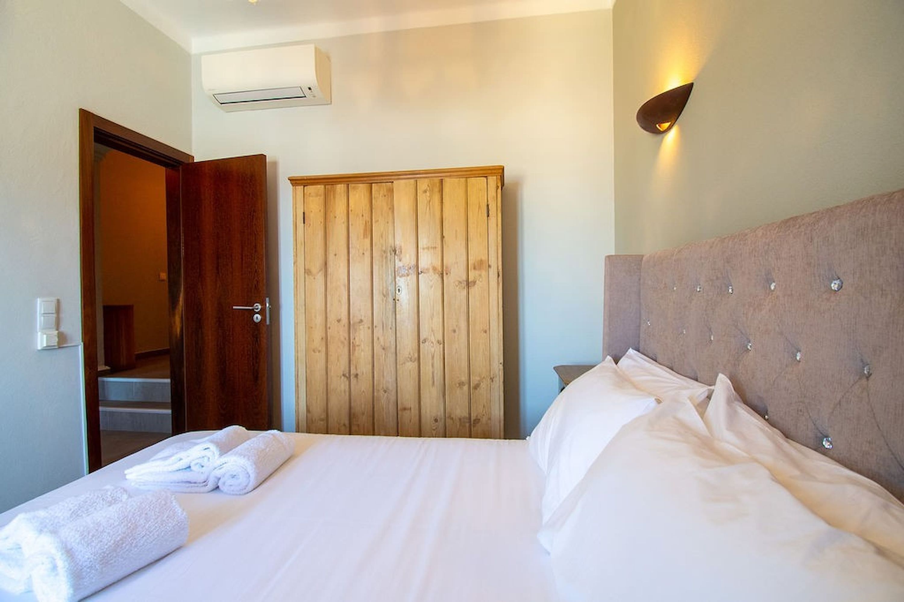 A hotel room with a bed, a wooden wardrobe, a door, and a wall-mounted light fixture.