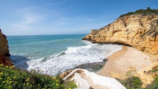 Eine Küstenlandschaft mit einem Sandstrand, felsigen Klippen und wolkenlosem, blauem Himmel.