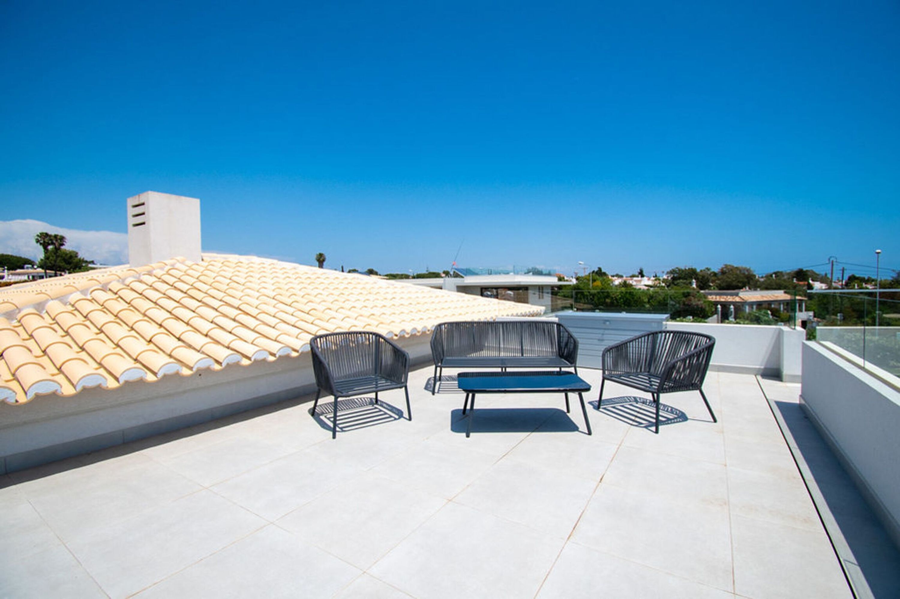 Une terrasse sur le toit, avec un toit recouvert de tuiles, un mur blanc et un ciel d’un bleu limpide.