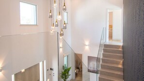 A modern staircase with glass railings, a hanging light fixture, and a potted plant. - Casa da Lua in Carvoeiro (Lagoa)