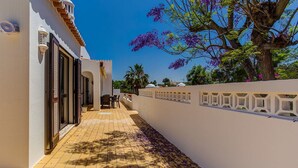 Un pasillo con piso de baldosas, pared blanca con diseño decorativo y un árbol con flores moradas.