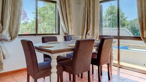 Un comedor con mesa y sillas, ventanas amplias y suelo de baldosas.