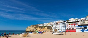Una spiaggia con barche, una scogliera e edifici con insegne come 'Don Carvoeiro'.