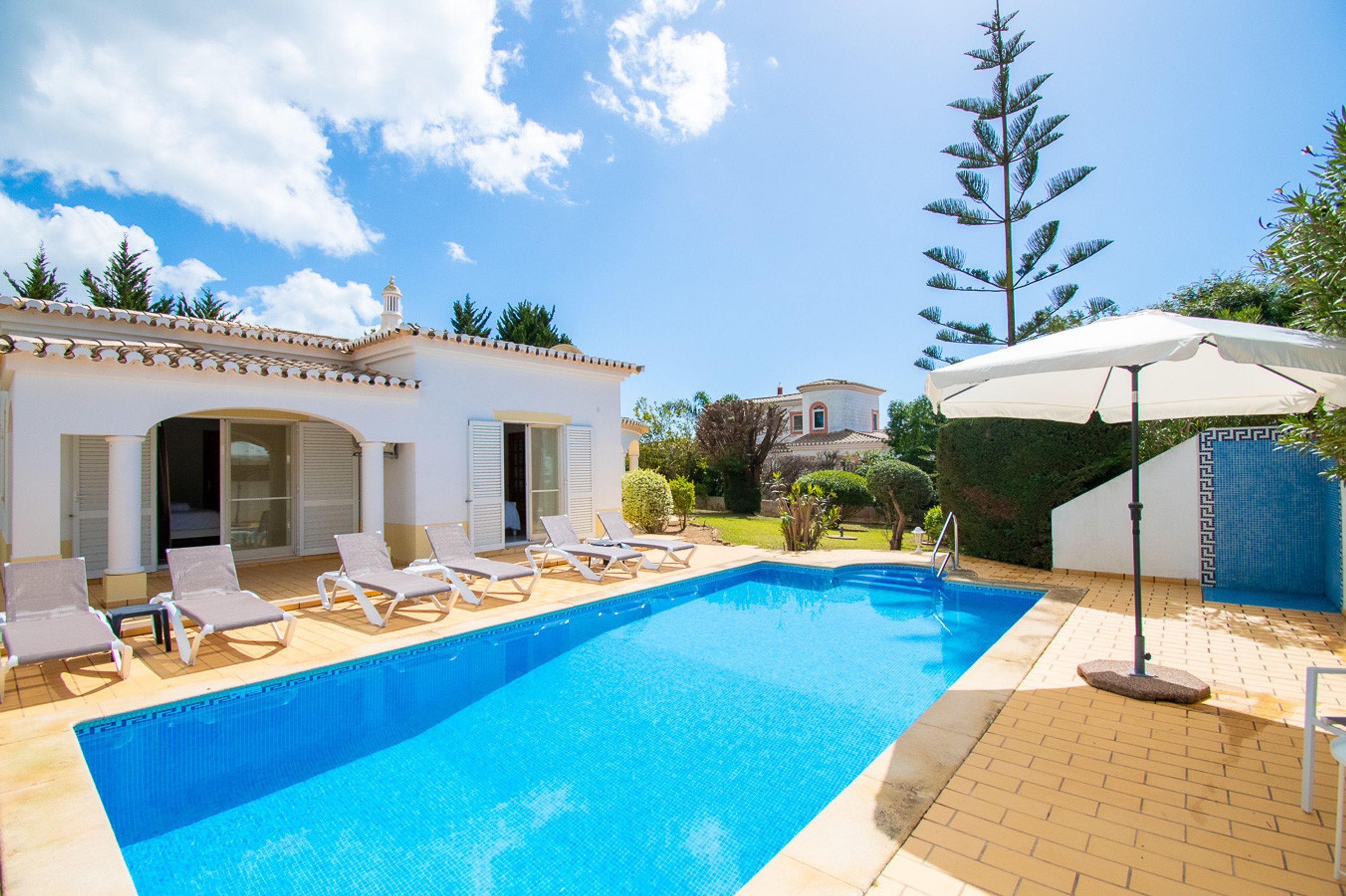 A swimming pool with lounge chairs, a patio area, and a building with a tiled roof.