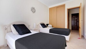 Een hotelkamer met twee bedden, een houten garderobe en een klein nachtkastje met een lamp.