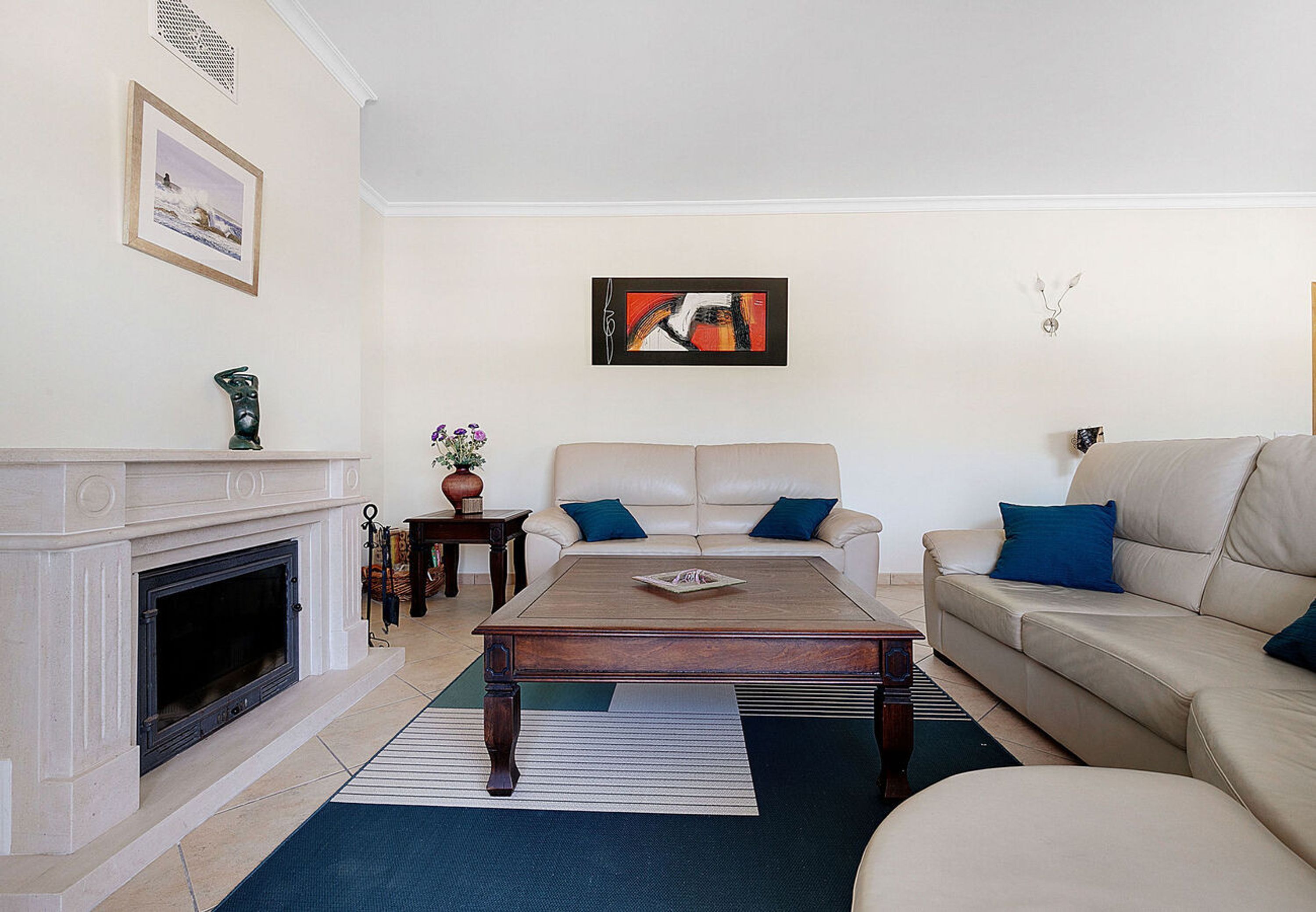 A living room with a fireplace, a beige sofa, a coffee table, and a painting on the wall.
