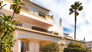 A two-story building with a balcony, a palm tree, and a small garden area with chairs. - 54 Golf mar Carvoeiro Apartment With Fabul (Lagoa)