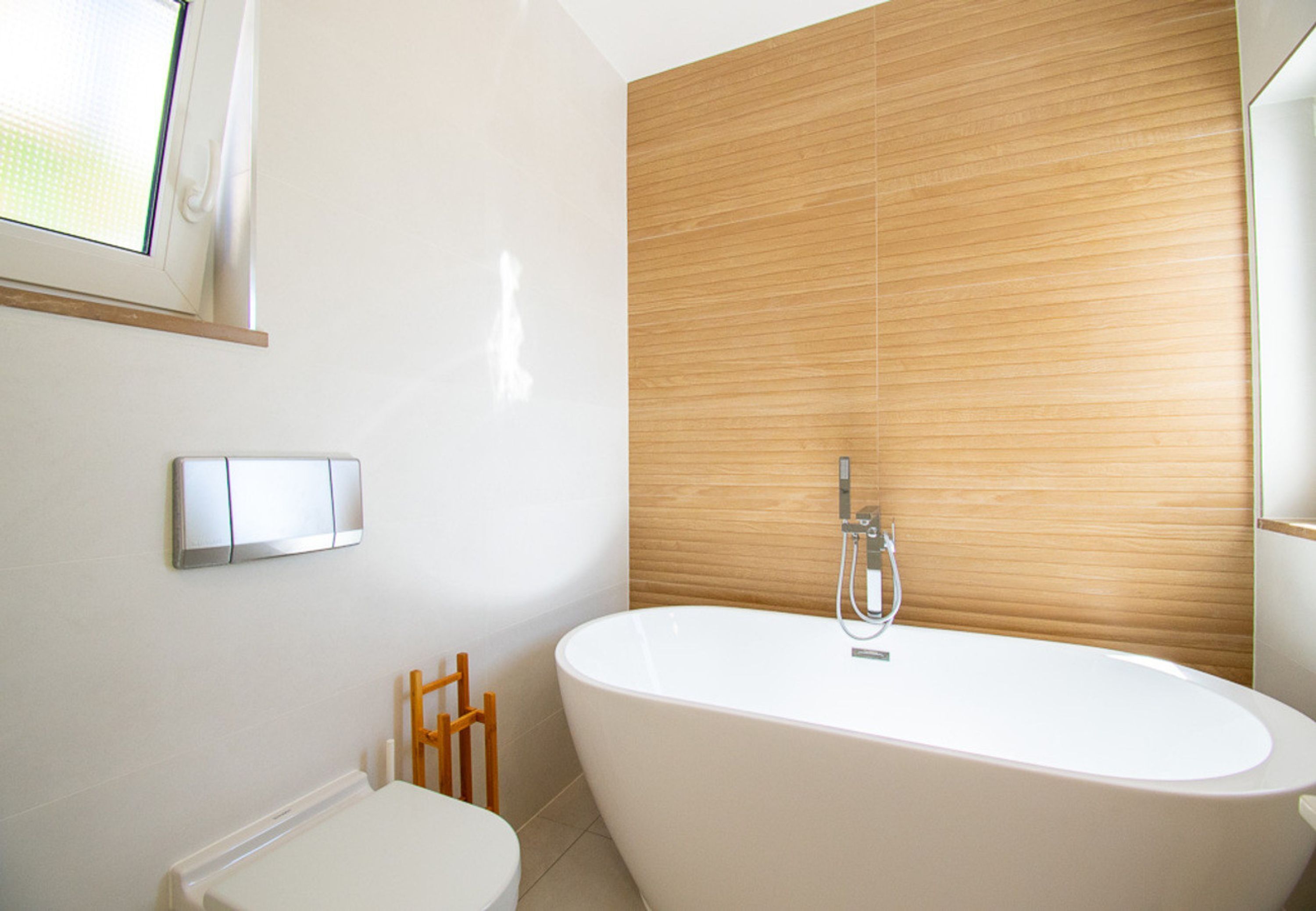 A modern bathroom with a freestanding bathtub, a toilet, and a wooden panel wall.