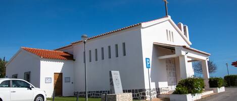 A white church with a red-tiled roof, a parking sign, and a cobblestone street.