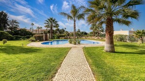 A landscaped garden with a circular pool, palm trees, and a paved walkway. - 99b Aldeia Golfmar Superb 2-bedroom Apartment (Lagoa)