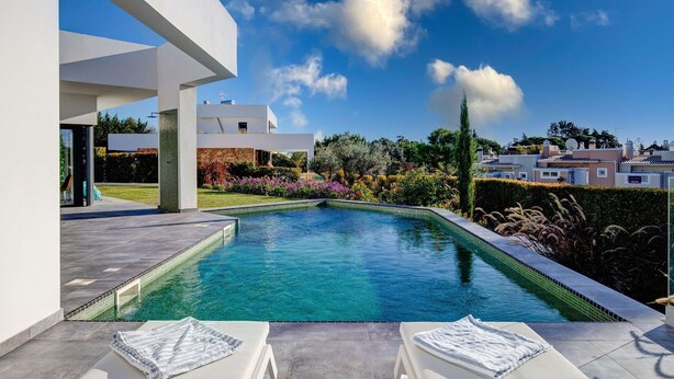 A modern pool area with clear blue water, white lounge chairs, and a view of surrounding houses and greenery. - Casa Blanca Magnificent 4 Bedroom Villa With MOD (Lagoa)