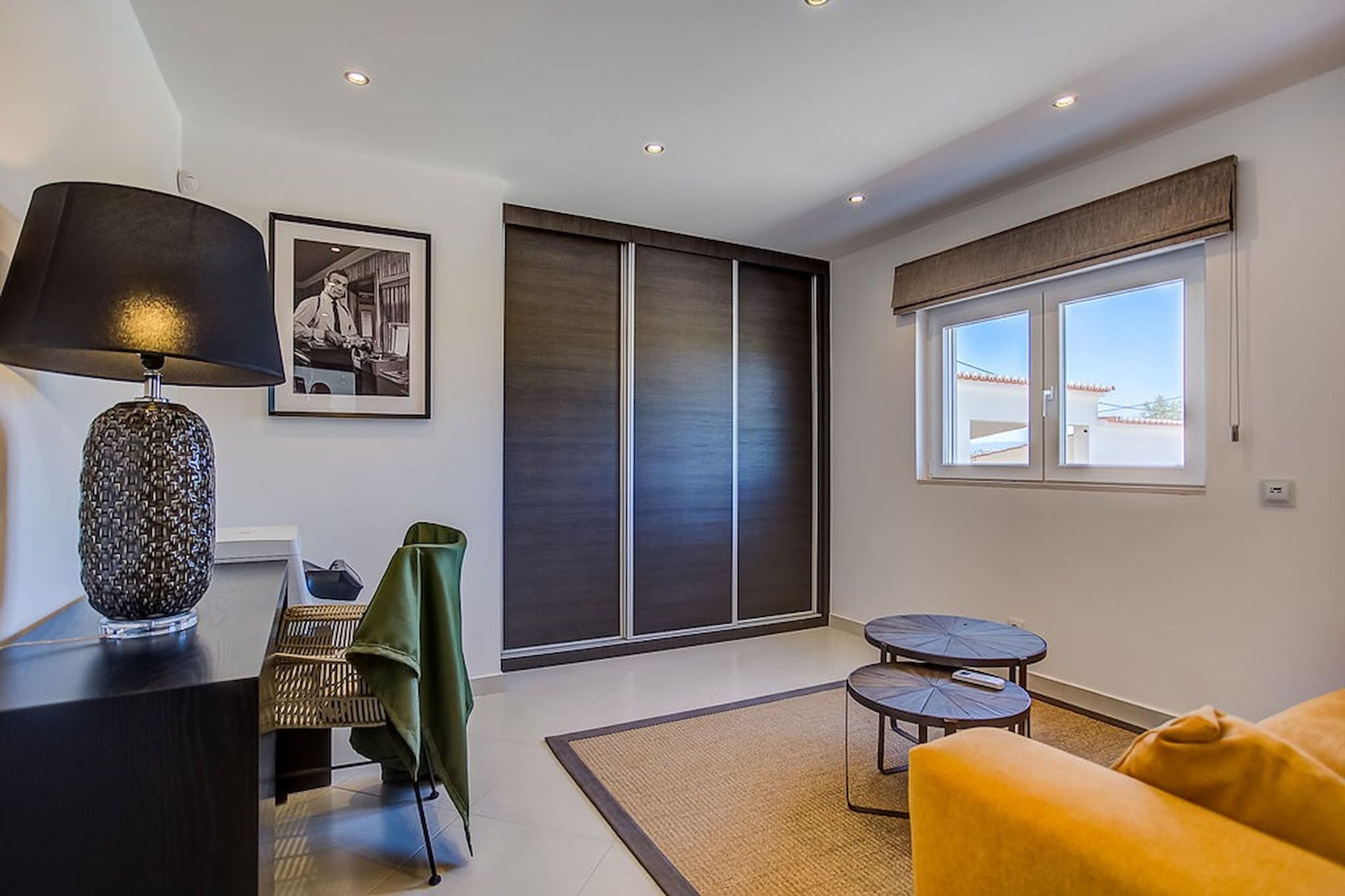Ein modernes Wohnzimmer mit Sofa, kleinem Tisch, Lampe, Sessel, einer großen Schiebetür und einem gerahmten Bild an der Wand.