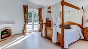 A spacious bedroom with a four-poster bed, a fireplace, and a large window with curtains. - Villa Barlavento in Carvoeiro (Lagoa)