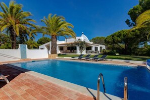A swimming pool with a tiled deck, lounge chairs, and palm trees. - Villa Barlavento in Carvoeiro (Lagoa)