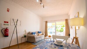 Un salon comprenant un canapé, une table basse, une table à manger avec des chaises, une lampe et un extincteur fixé au mur.