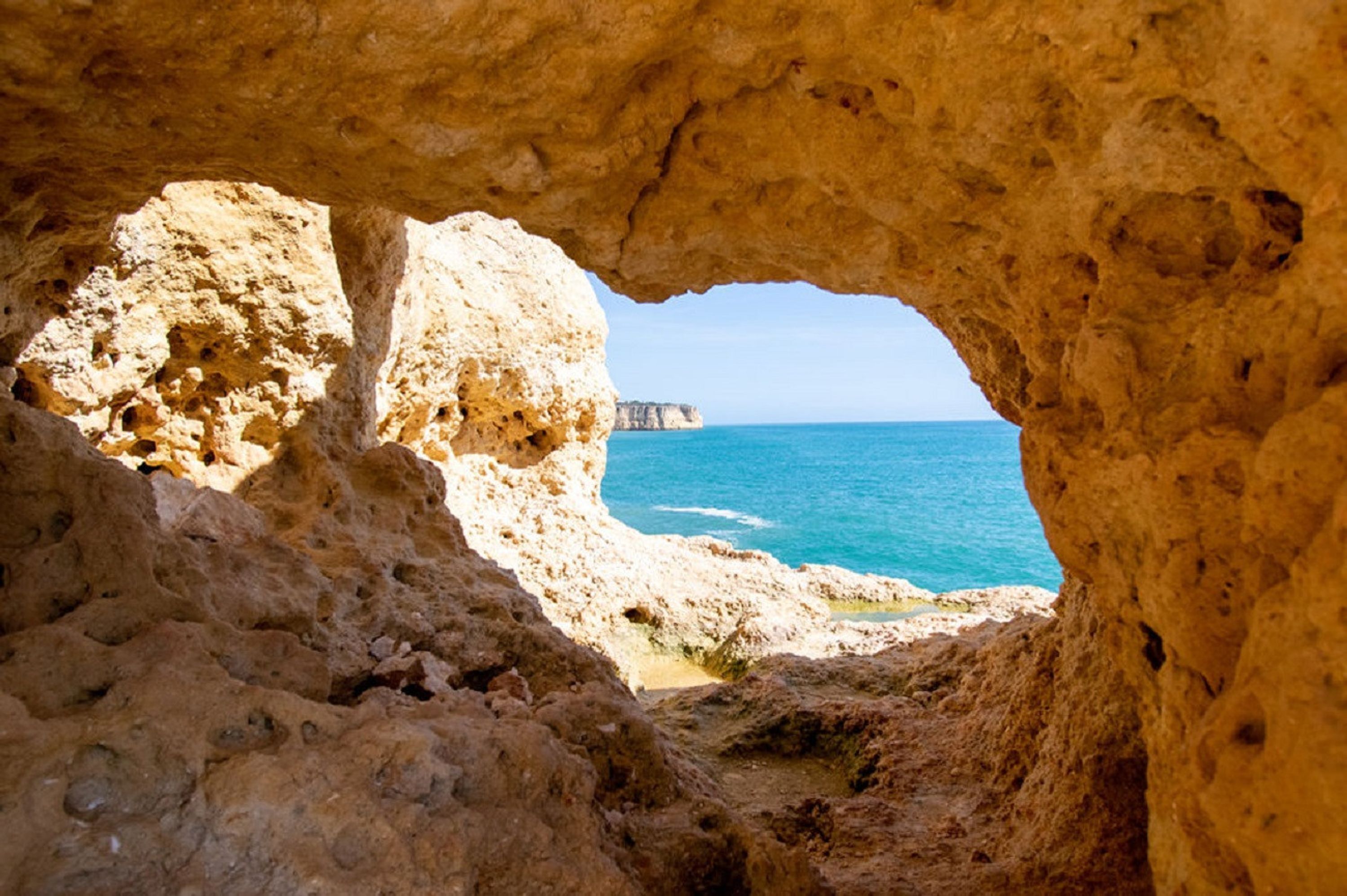 Eine natürliche Höhlenöffnung mit Blick auf das Meer und eine ferne Klippe.