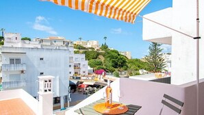 Un balcon avec un auvent rayé, une table avec une bouteille et un verre, et une chaise.