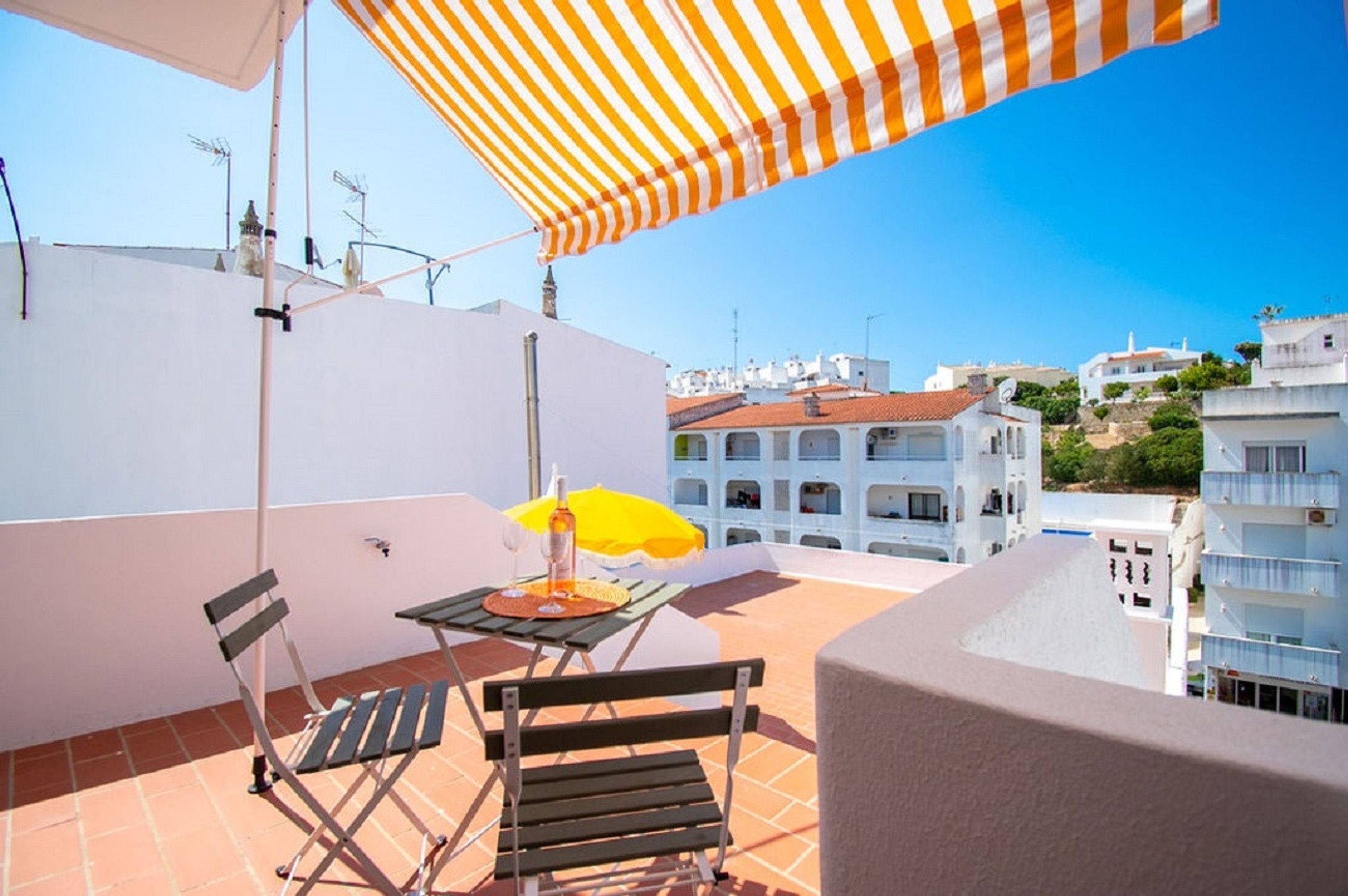 A rooftop terrace with a table, chairs, and a striped umbrella.