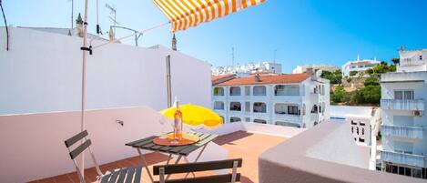 A rooftop terrace with a table, chairs, and a striped umbrella.
