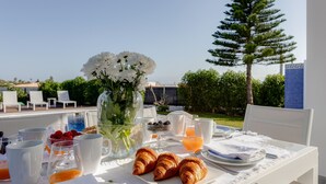 A breakfast table set with croissants, fruit, and beverages, overlooking a pool and greenery. - 125 Quinta do Paraiso - Casa Jacqueline (Lagoa)