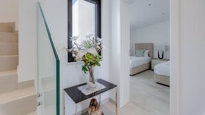 A modern bedroom with a large bed, a bedside table with a vase of flowers, and a staircase with a glass railing. - 125 Quinta do Paraiso - Casa Jacqueline (Lagoa)
