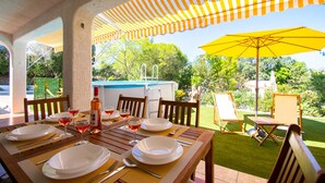 Un patio al aire libre con una mesa lista para comer, rodeada de sillas y cubierta por sombrillas amarillas a rayas y de color sólido.