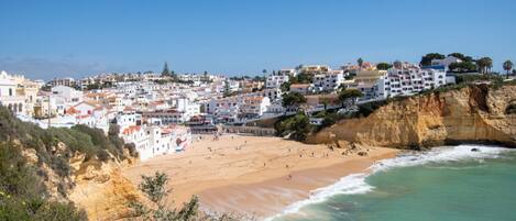 A coastal town with buildings on a cliff overlooking a sandy beach.