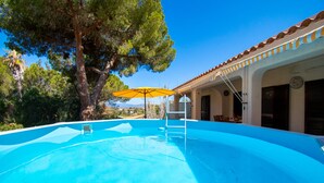 Una piscina con escalera, sombrilla y un edificio con techo de azulejos y columnas.