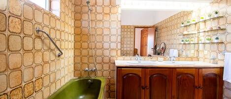 A bathroom with a green bathtub, wooden cabinets, a white sink, and a tiled wall with a window.